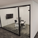 Floor-to-ceiling glass huddle room with black frame finish and frameless glass swing door #1649